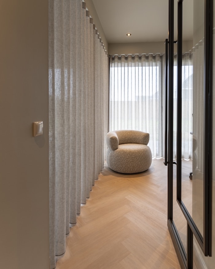 Zithoek met ronde designfauteuil en lichtdoorlatende gordijnen op visgraatvloer
