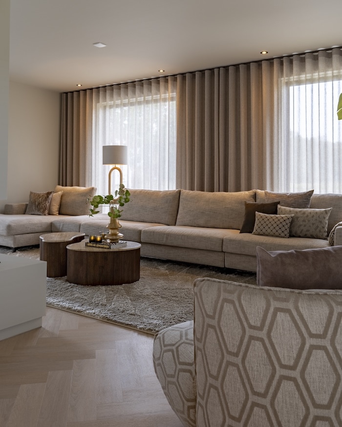 Sfeervolle zithoek met beige hoekbank, ronde houten salontafels en warme accenten