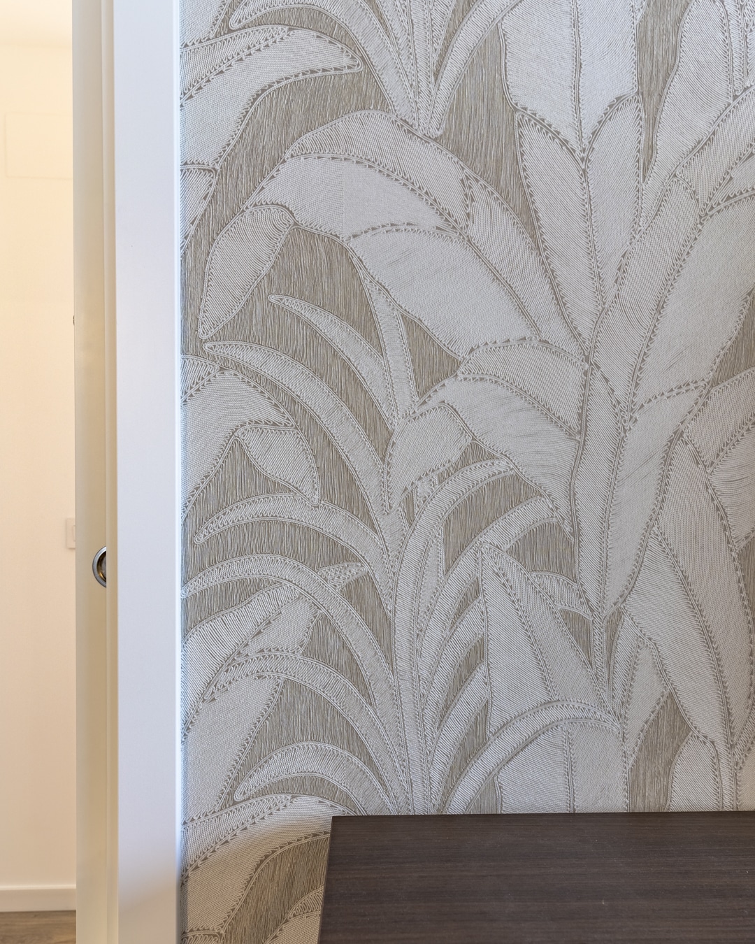 Close-up van luxe Arte behang met tropisch bladmotief in neutrale tinten, als stijlvol accent in de woonkamer