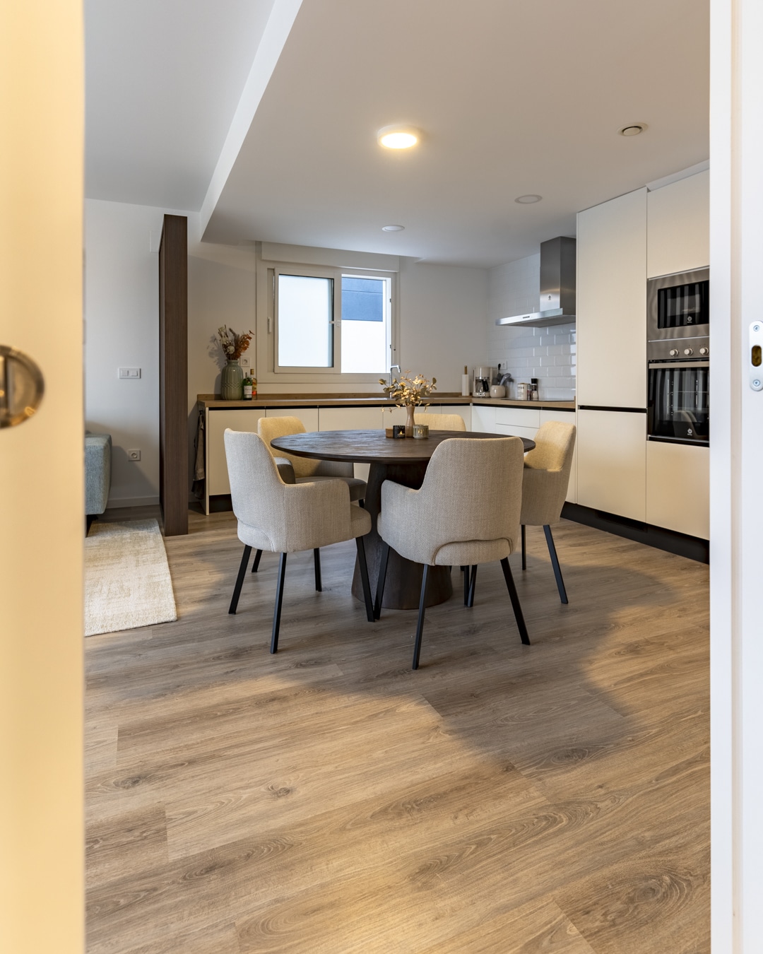 Doorkijk naar de keuken en ronde eettafel met comfortabele stoelen, uitgevoerd in warme materialen