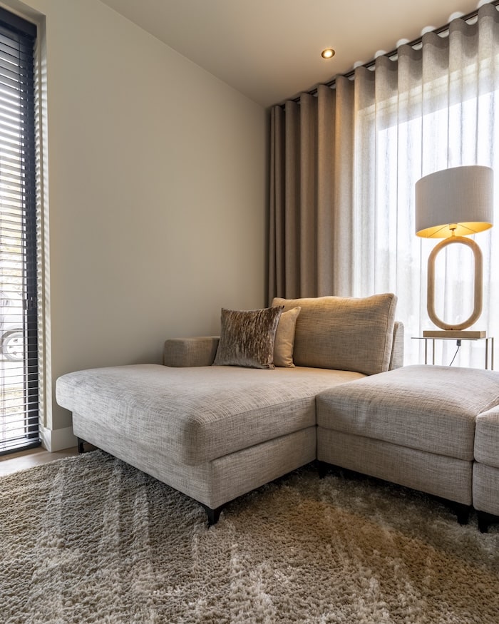 Comfortabele loungebank met chaise longue en tafellamp naast het raam met vitrage