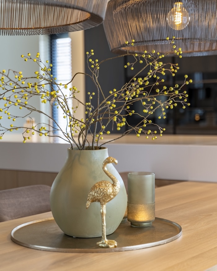 Styling met groene vaas, takken en goudkleurig flamingobeeldje onder zwarte lampen