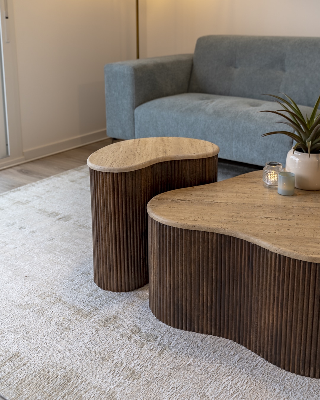 Twee organisch gevormde salontafels met ribbelstructuur en travertin blad op een licht vloerkleed