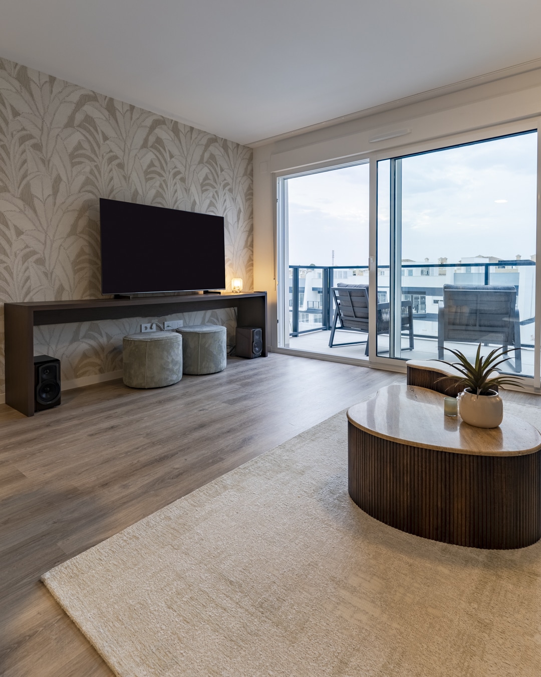 Woonkamer met schuifpui naar het balkon, zachte vloerkleden en houten salontafel.