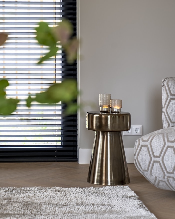 Gouden design bijzettafel met sfeervolle kaarsen, naast fauteuil met geometrisch patroon