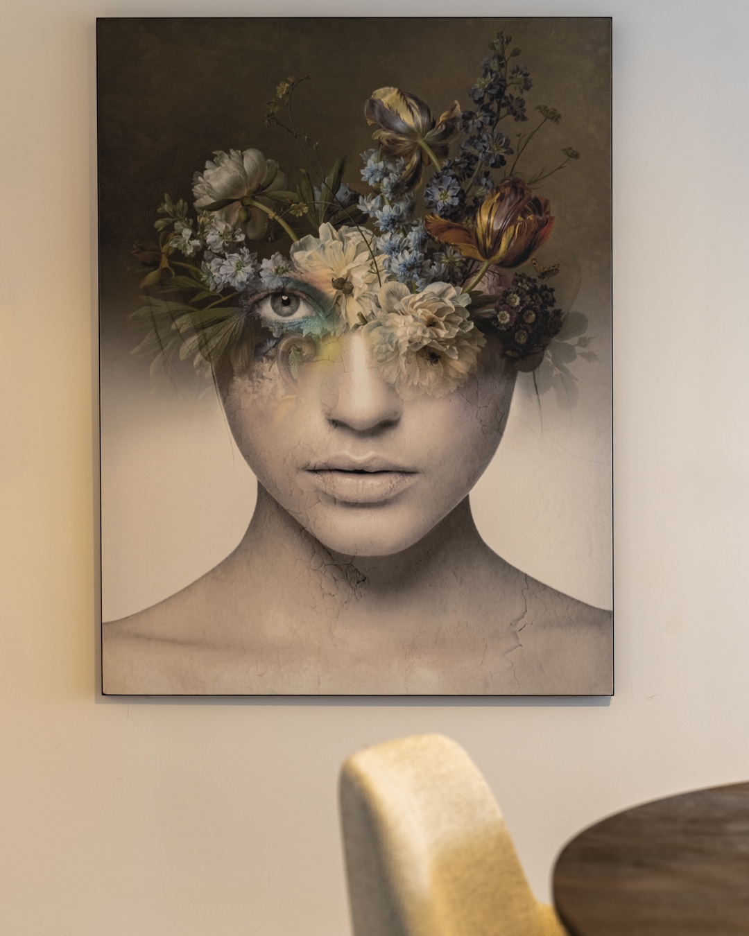 Close-up van een kunstwerk met een vrouwengezicht en kleurrijke bloemen op een witte muur.