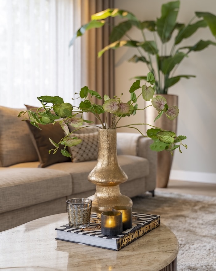 Decoratieve gouden vaas met bladgroen, glazen kaarsenhouders en stijlboek in natuurlijke setting