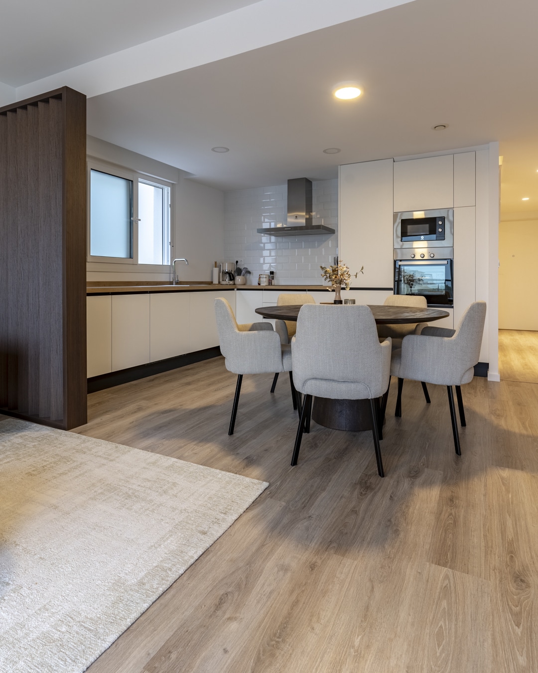 Open keuken met ronde eettafel, beige stoelen en doorkijk naar zithoek.