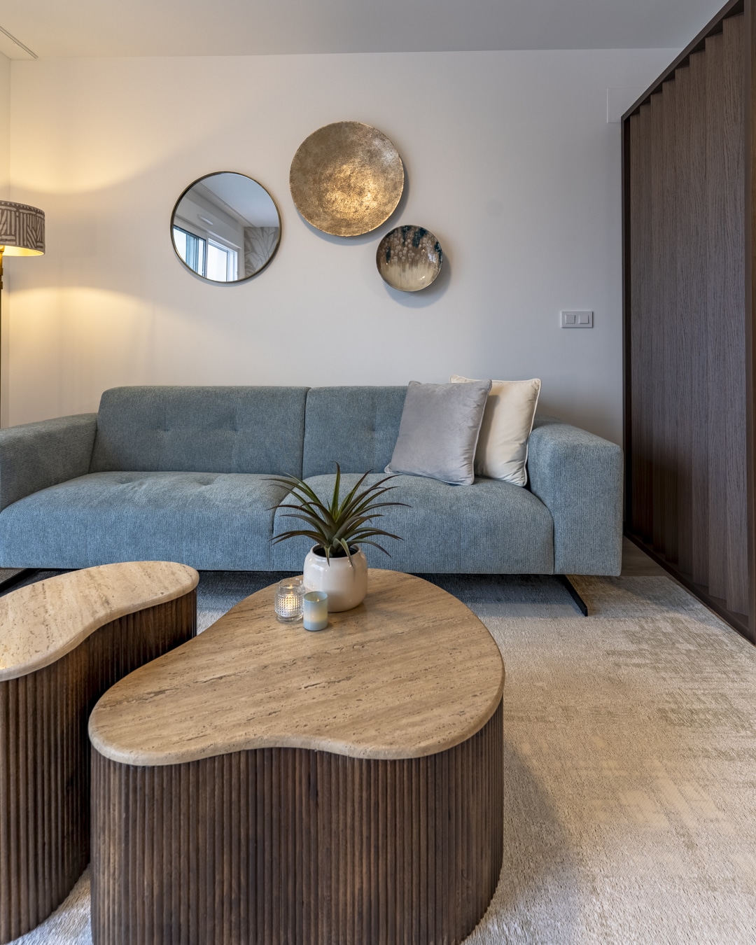 Organisch gevormde salontafels op vloerkleed met comfortabele bank en wanddecoratie.