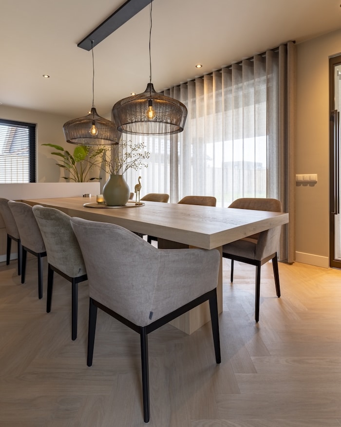 Eethoek met lange houten tafel en comfortabele armstoelen bij grote ramen met vitrage