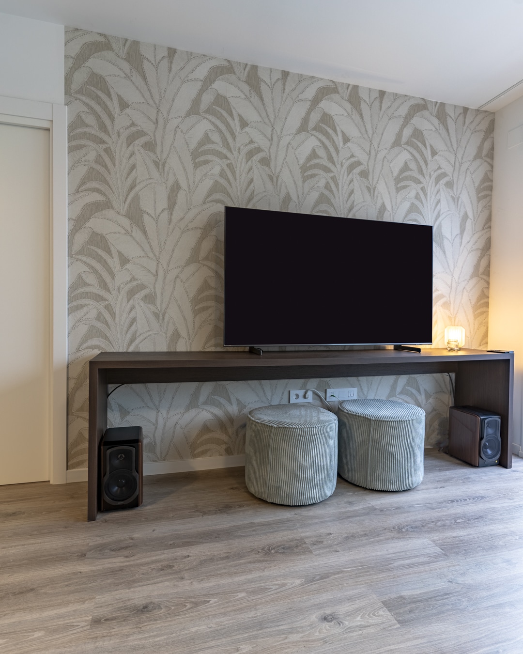 Televisiewand met botanisch Arte behang, houten meubel en twee poefs in ribfluweel.