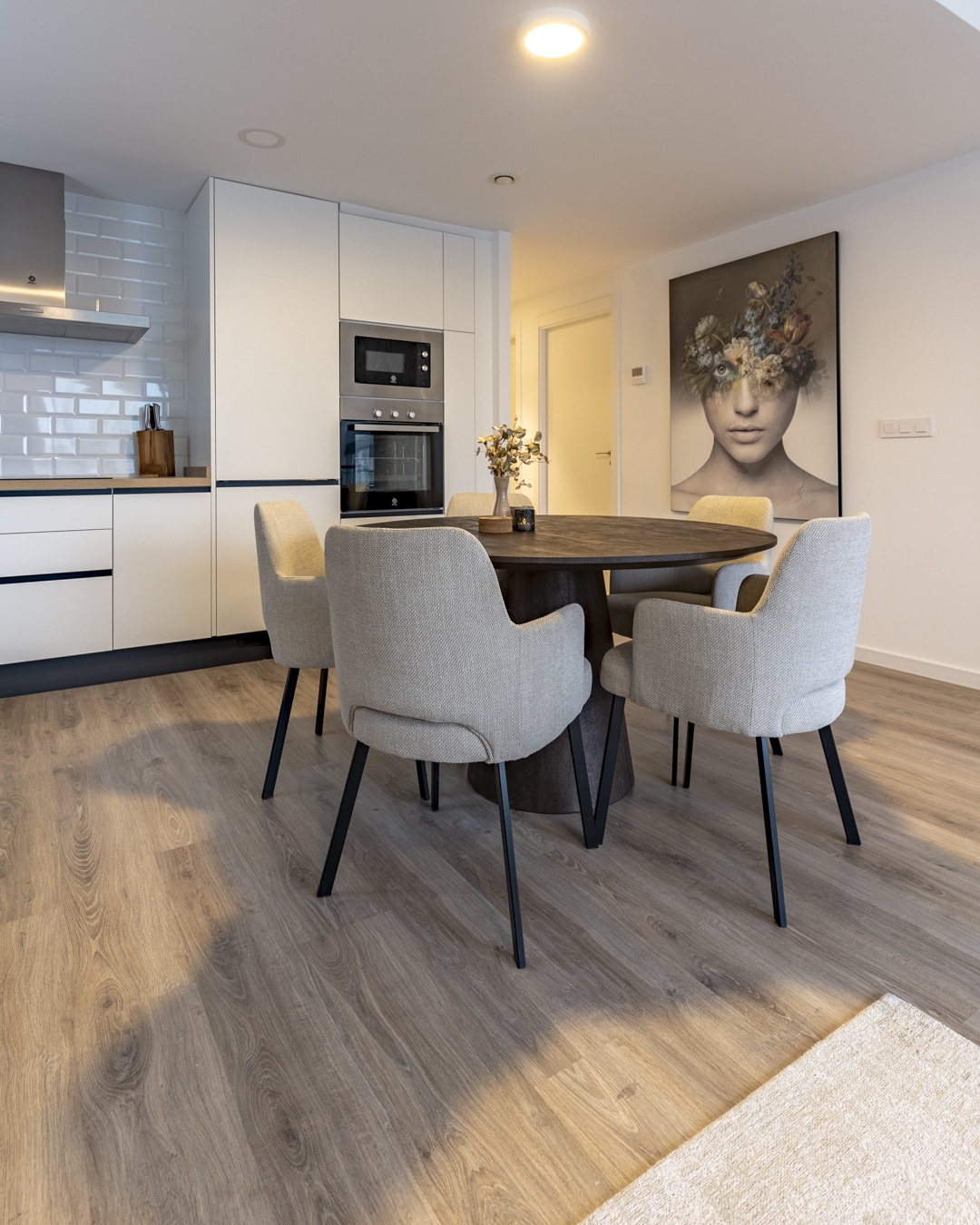 Eethoek met kunstwerk aan de muur, zachte stoelen en houten vloer.