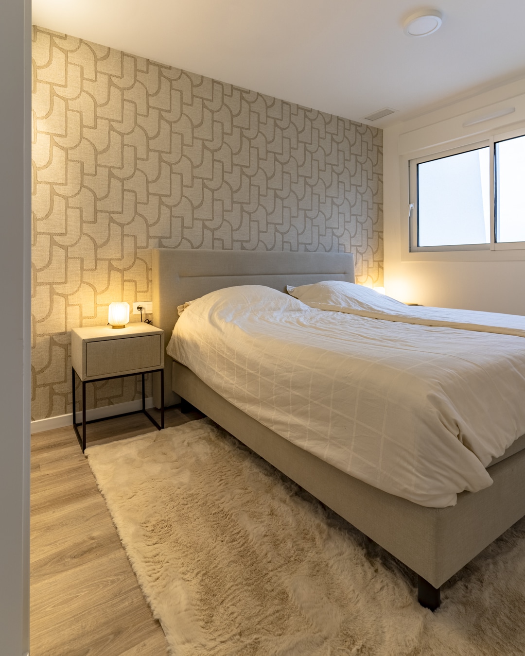 Slaapkamer met Arte behang, zacht vloerkleed en nachtkastje met sfeerlamp.