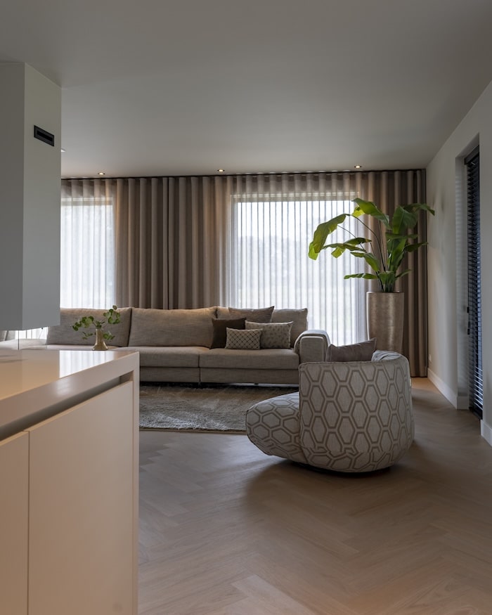 Lichte woonkamer met ronde fauteuil, lange bank en kamerplanten bij raam