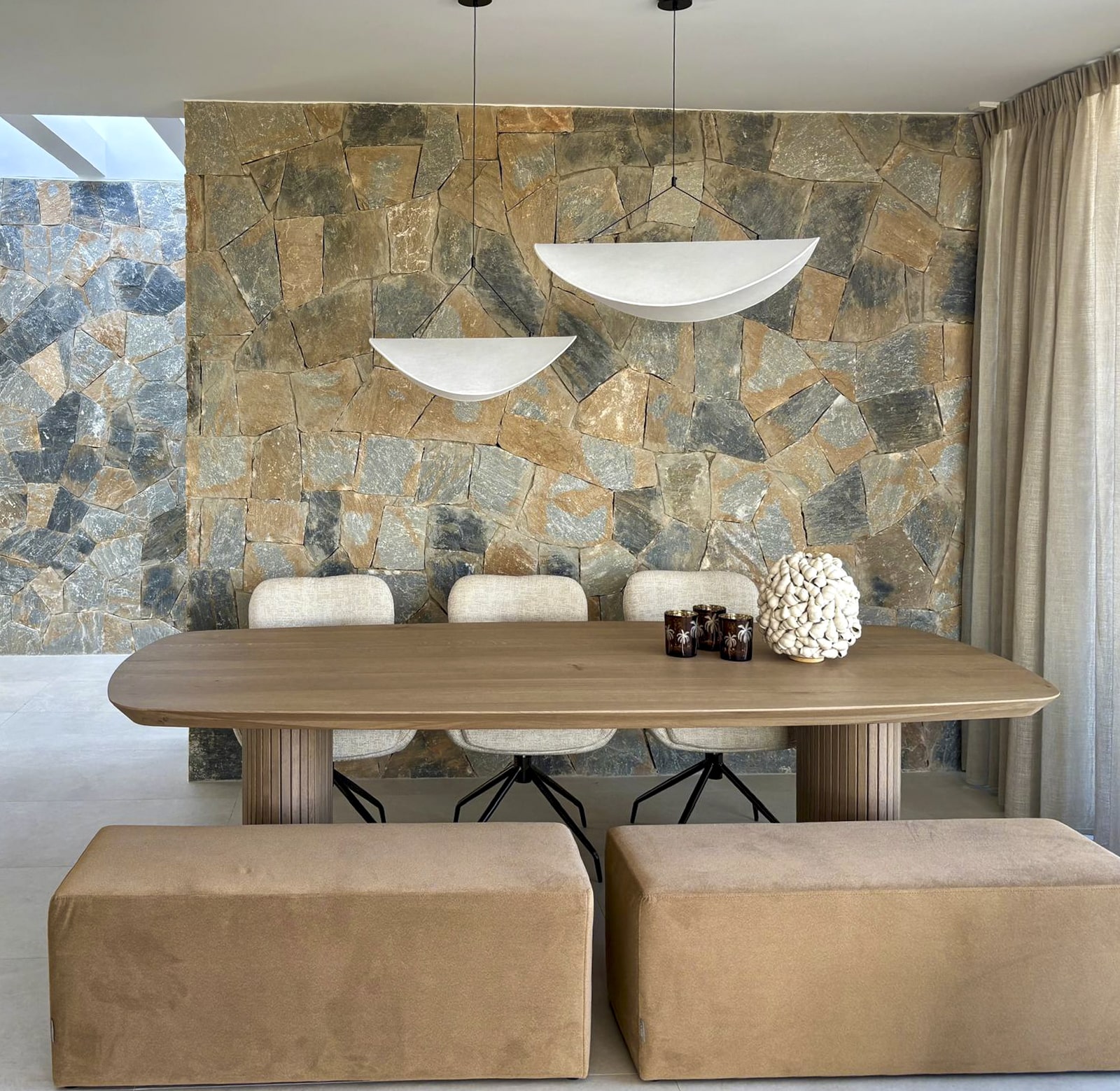 Modern ingerichte eetkamer met houten eettafel, stoffen zitbank, comfortabele stoelen en een natuurstenen muur als krachtig stijlstatement, gecombineerd met kunstzinnige verlichting.