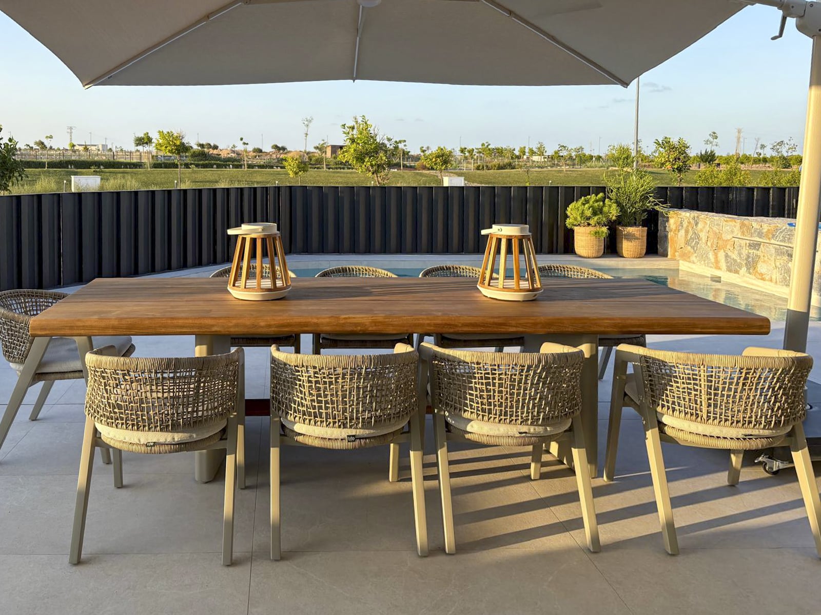 Luxe buitenruimte met grote houten eettafel, gevlochten stoelen en uitzicht op het zwembad in Spaanse villa