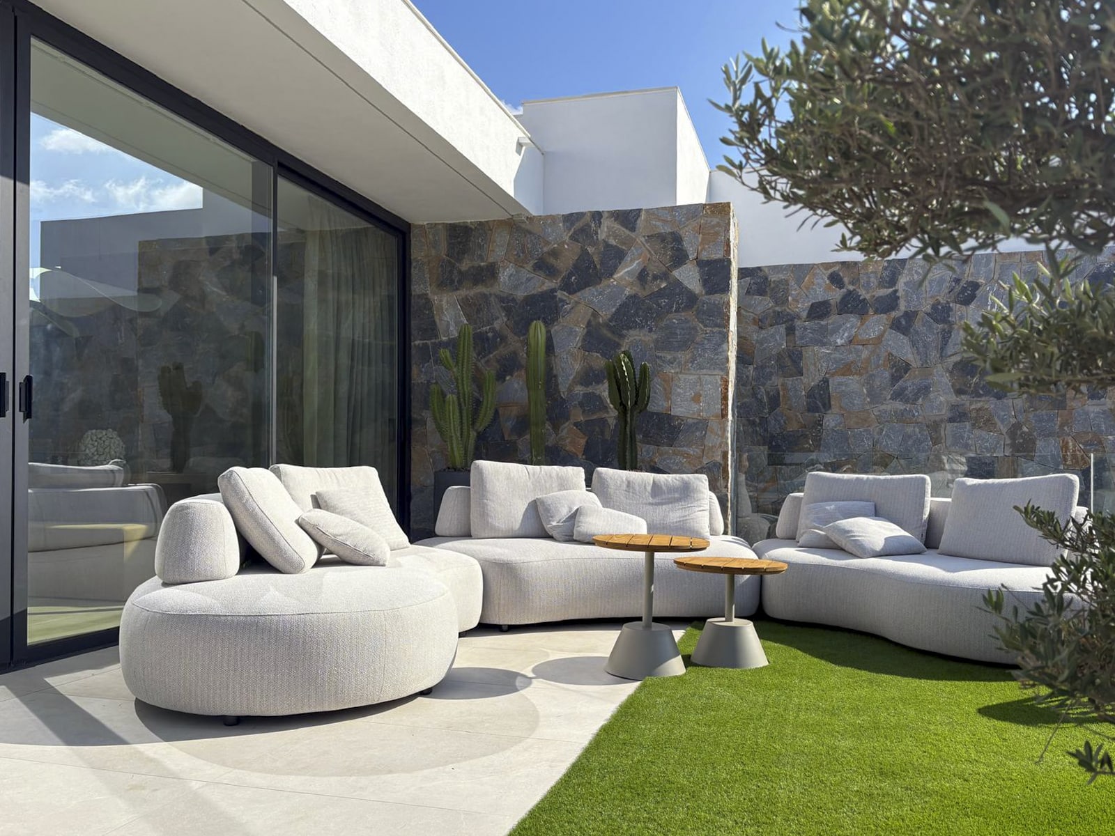 Stijlvolle buitenlounge met witte banken, groene kunstgrasmat en natuurlijke planten
