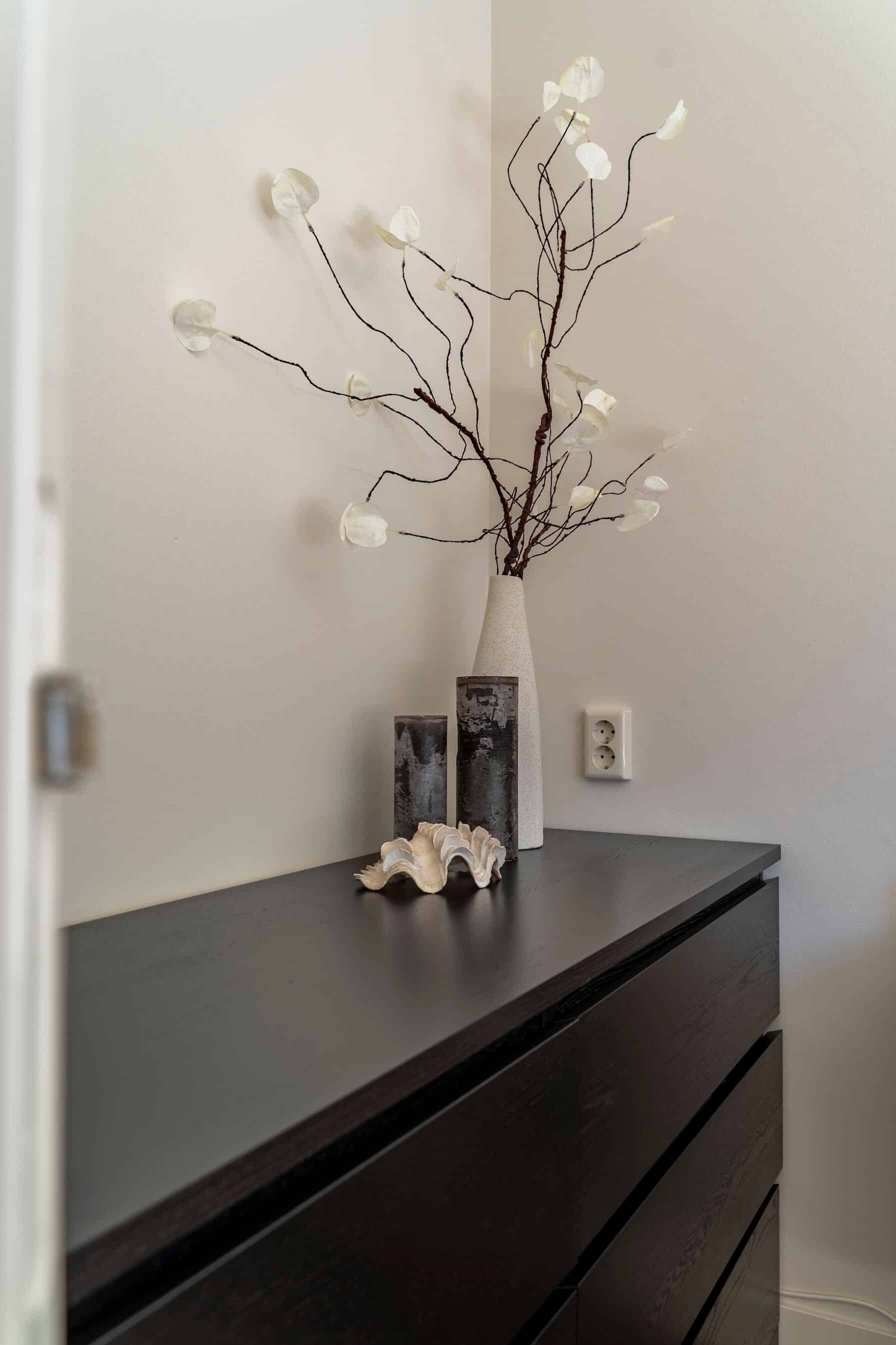 Witte vaas met takken en stijlvolle objecten op een donkerhouten dressoir