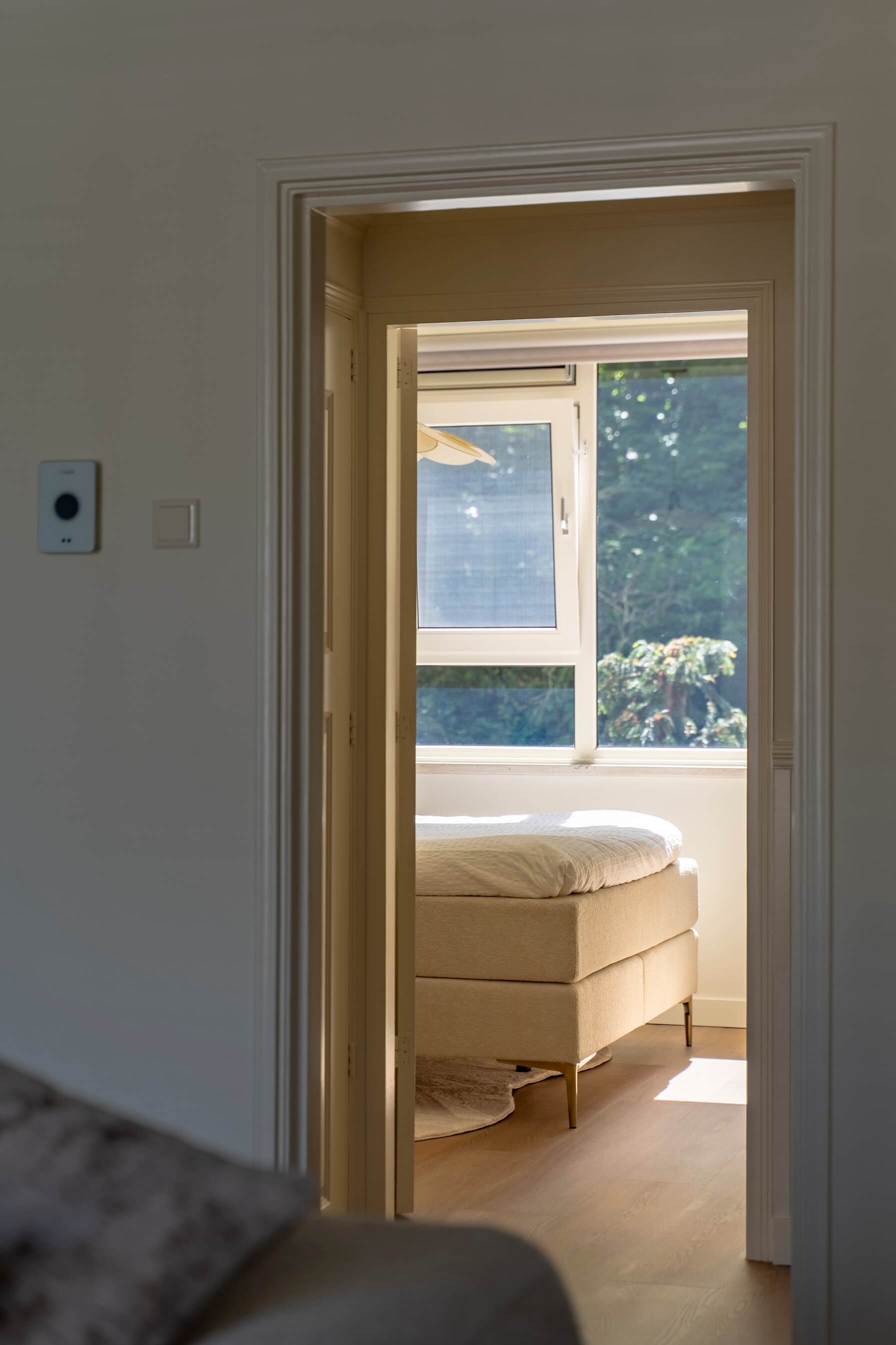 Zicht vanuit de woonkamer op de lichte slaapkamer, met zonlicht dat naar binnen valt