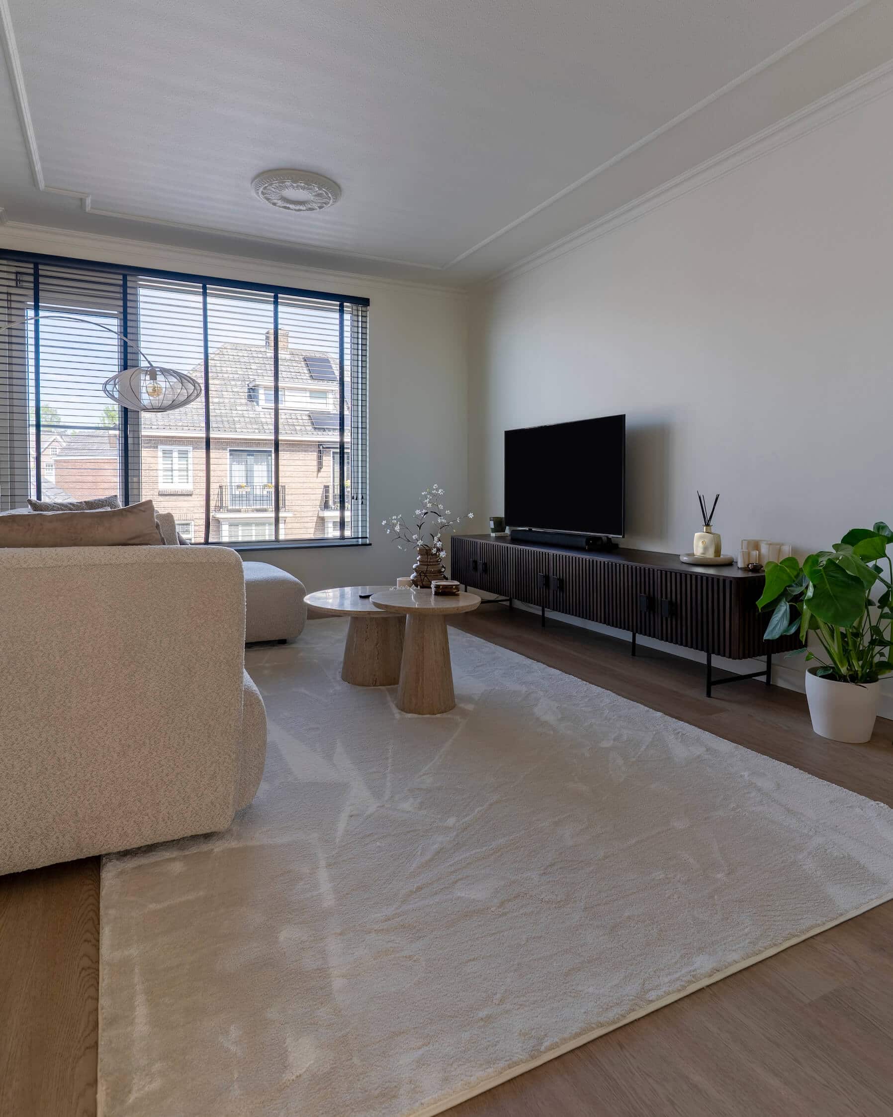 Grote ramen met zwarte jaloezieën, zachte vloerkleed en moderne tv-kast in een sfeervol interieur