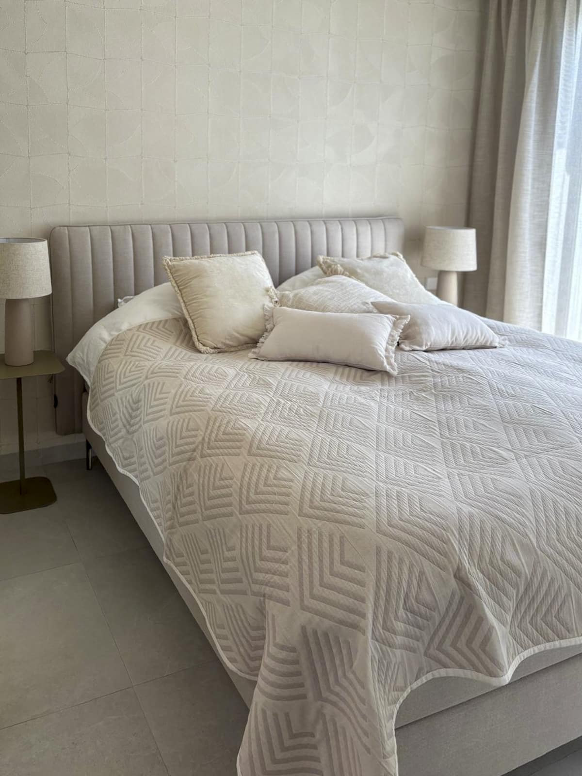 Tweepersoonsbed met zachte sprei, kussens en veel natuurlijk daglicht.