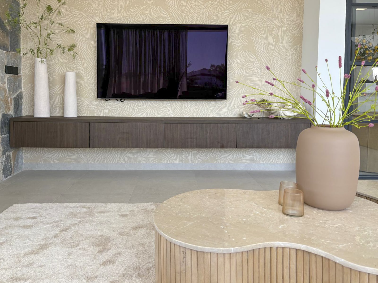 Woonkamer met minimalistisch tv-meubel, behang met palmprint en moderne styling.