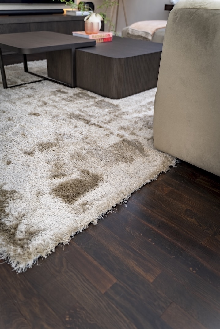 Luxe hoogpolig vloerkleed in beige tinten op donker houten vloer