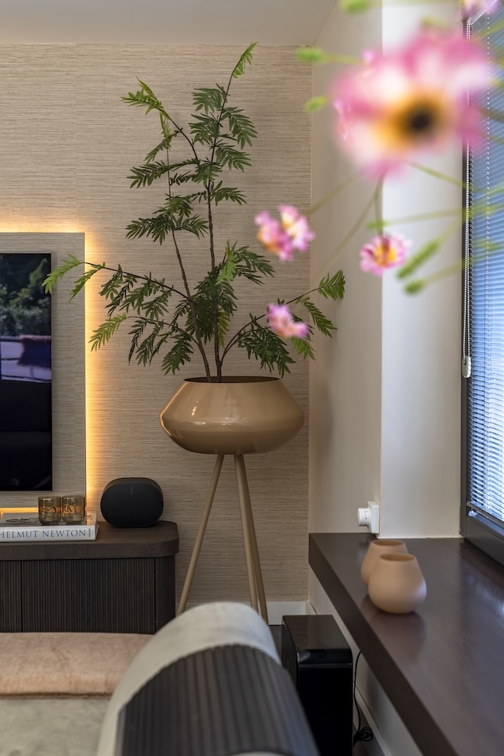 Grote design plantenpot op hoge poot naast tv-meubel met sfeervolle wandverlichting