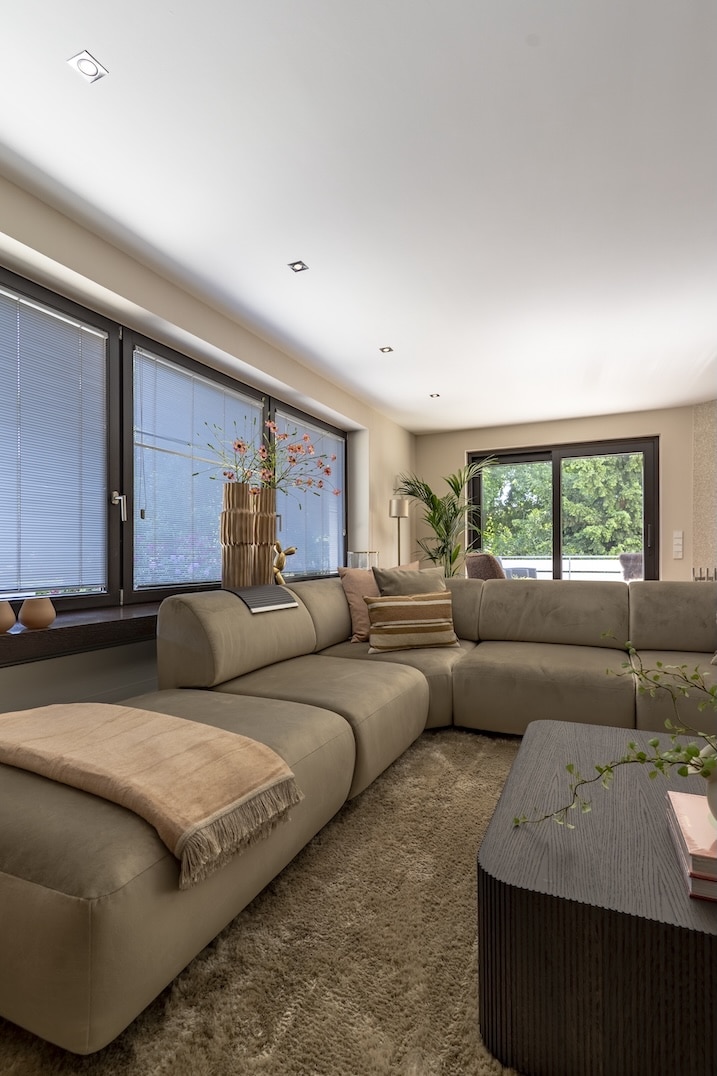 Comfortabele hoekbank met sierkussens, beige plaid en styling bij het raam