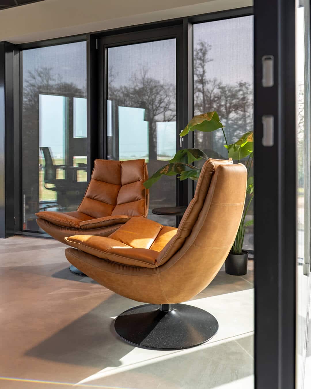 Luxe cognackleurige fauteuils bij grote raampartijen in modern bedrijfspand