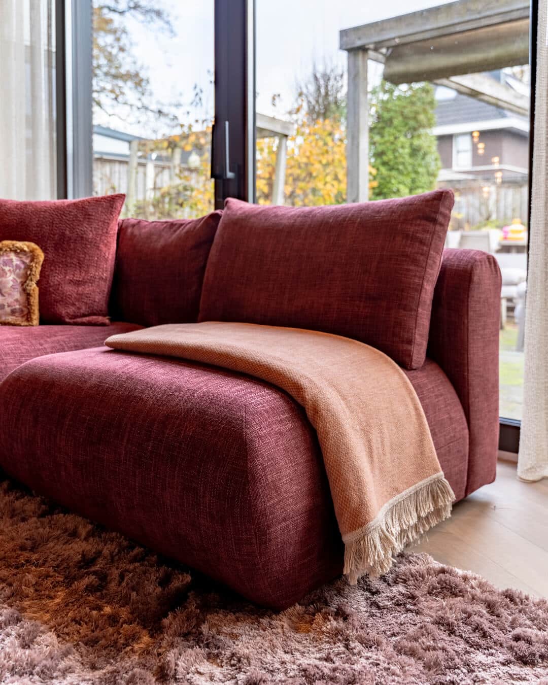 Detail van bordeauxrode hoekbank met zachte plaid in luxe woonkamer