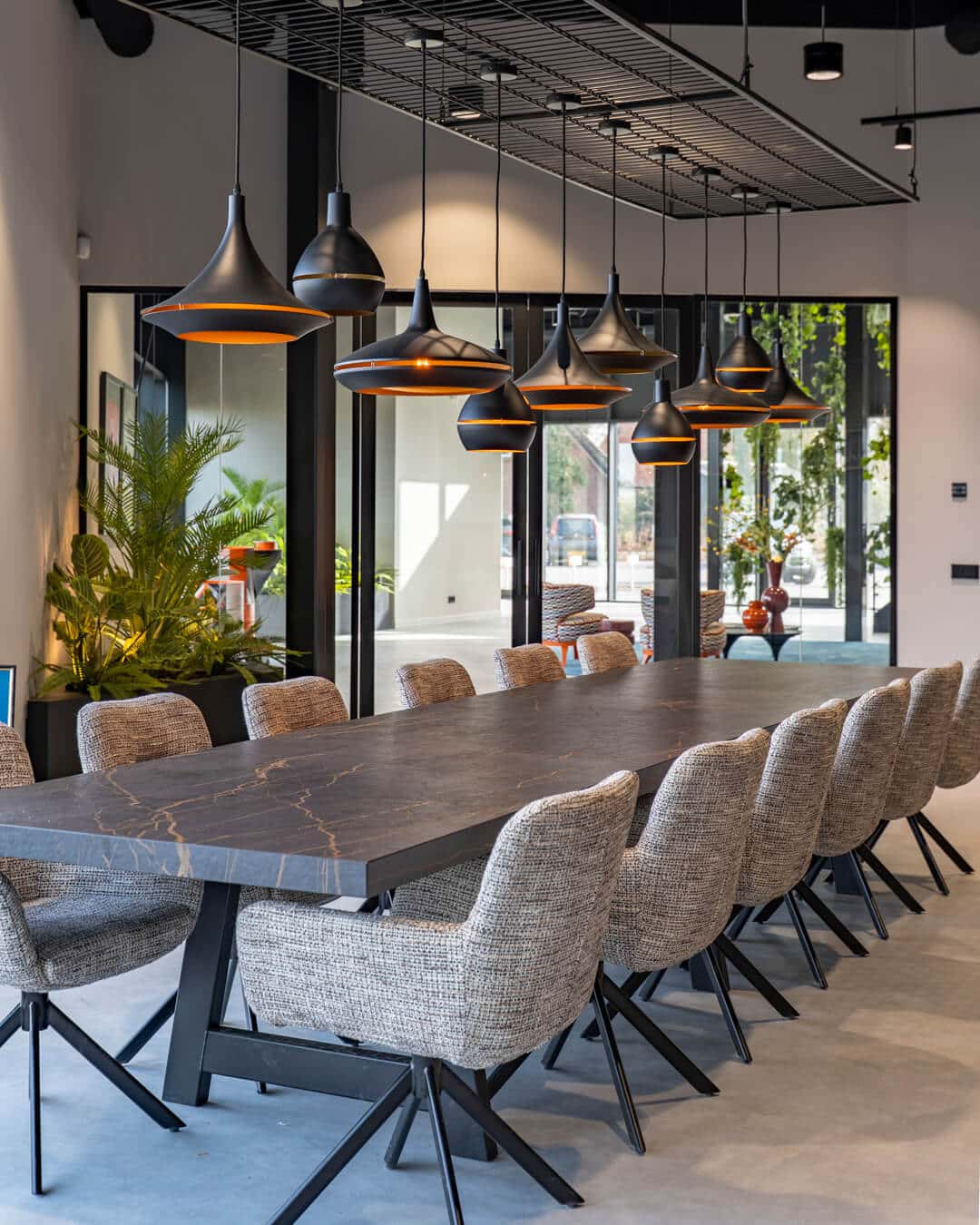 Grote gezamenlijke tafel met designstoelen en hanglampen in kantoorinterieur