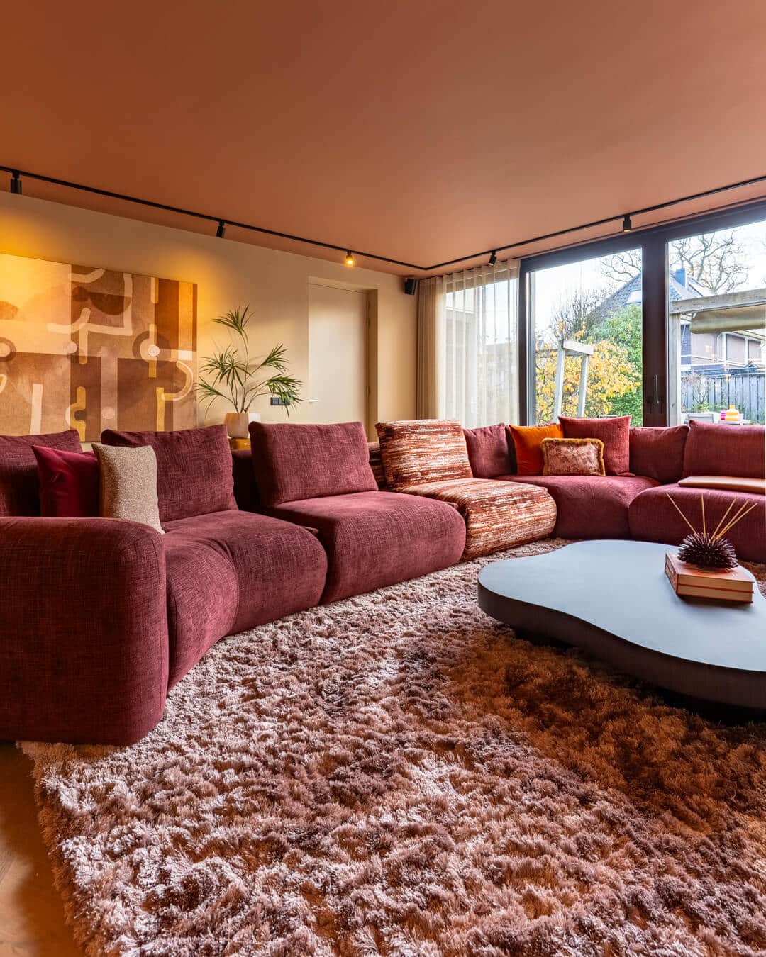 Royale bordeauxrode modulaire bank met kleurrijke sierkussens in luxe woonkamer