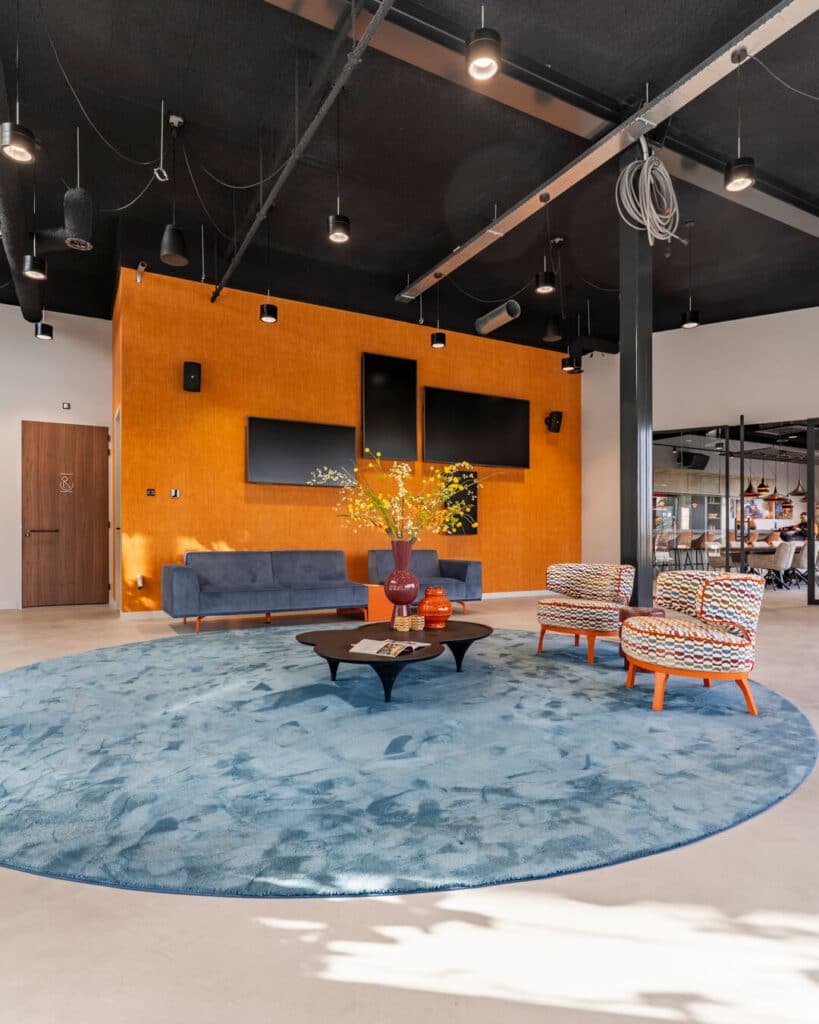 Kleurrijke lounge met blauw vloerkleed en oranje accentwand in kantoorinterieur