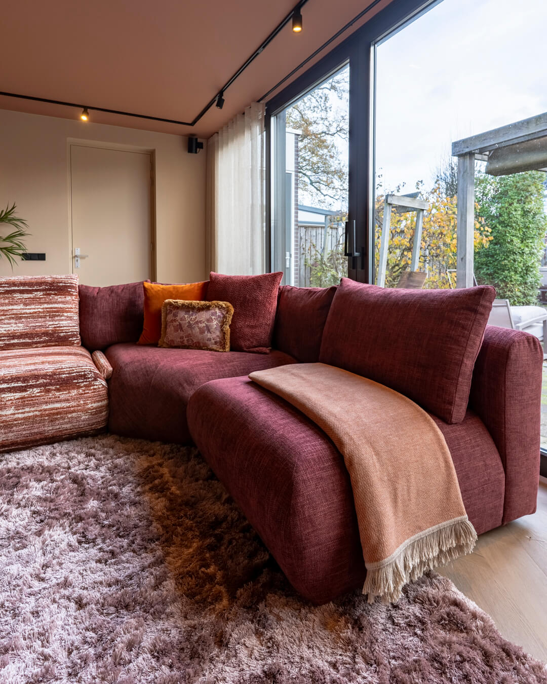 Detail van bordeauxrode hoekbank met zachte plaid en sierkussens