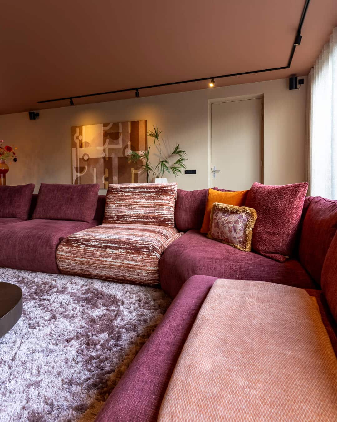 Bordeauxrode hoekbank met accentstoel en warme aardetinten in modern interieur