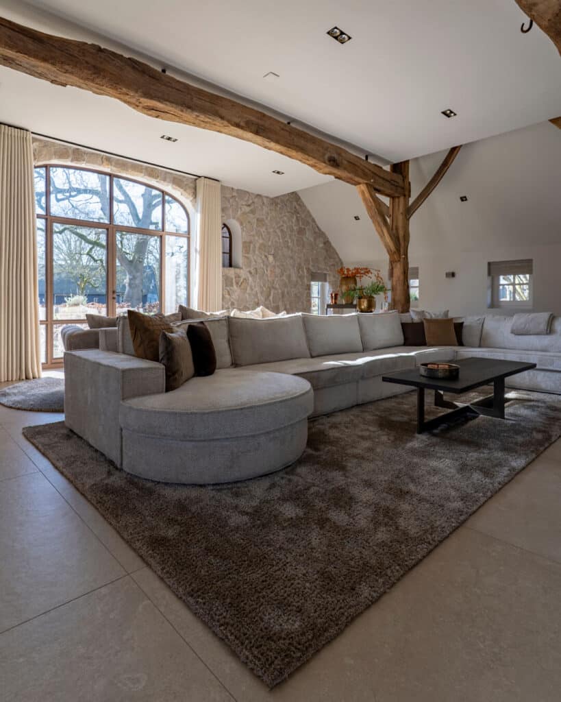 Monumentale boerderij met luxe woonkamer, houten balken, natuurstenen muren en royale organische bank.