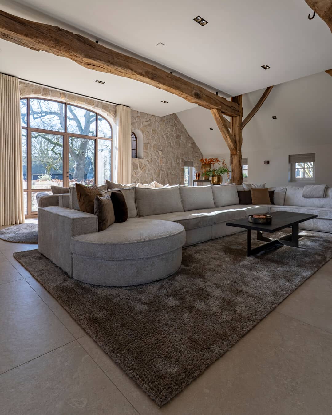 Monumentale boerderij met luxe woonkamer, houten balken, natuurstenen muren en royale organische bank.