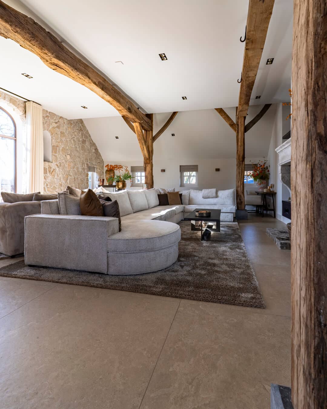 Sfeervolle woonkamer in rijksmonument met natuurstenen wand, houten gebinten en modern interieur.