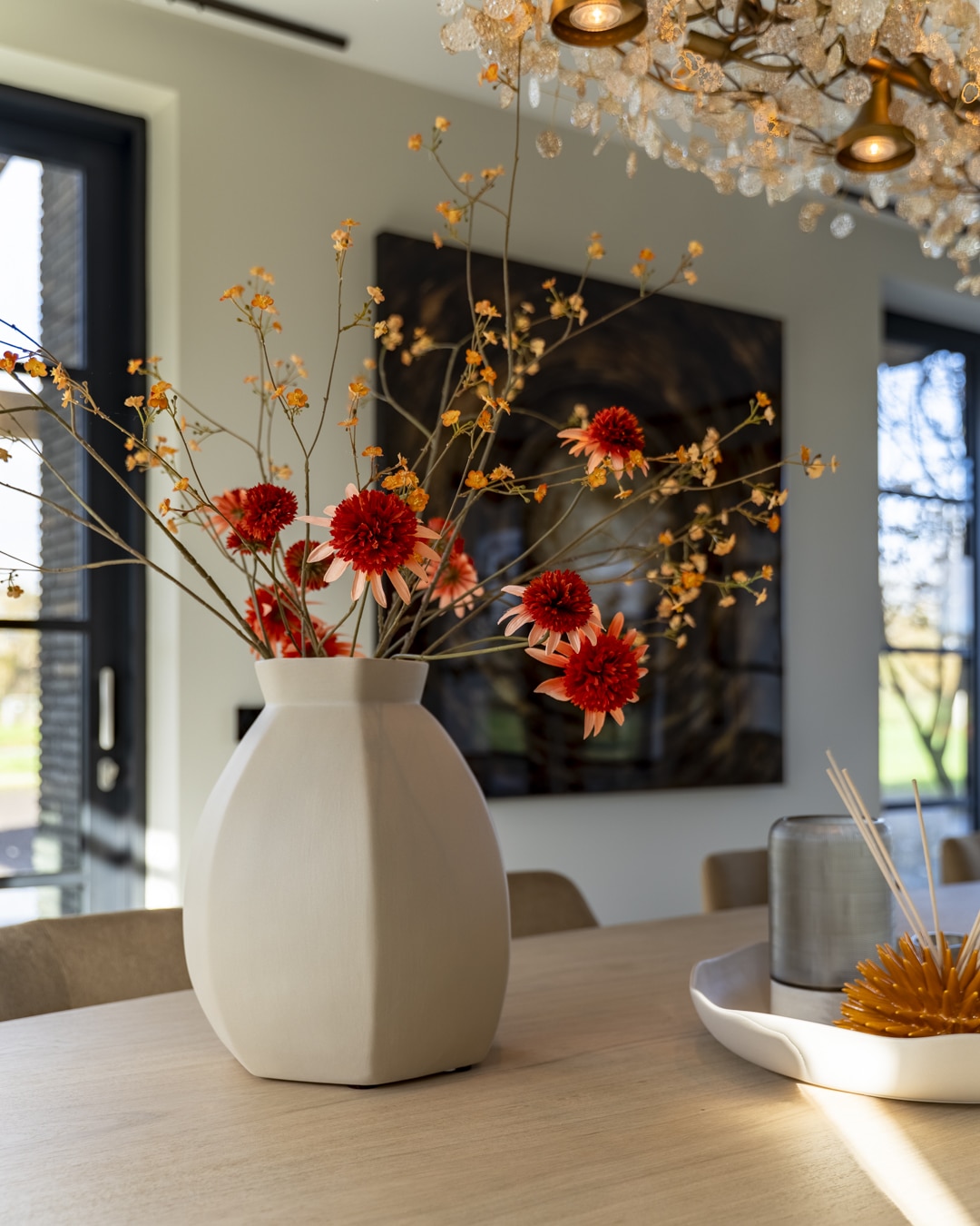 Grote vaas met kleurrijke bloemen als warm accent op de ovale eettafel.