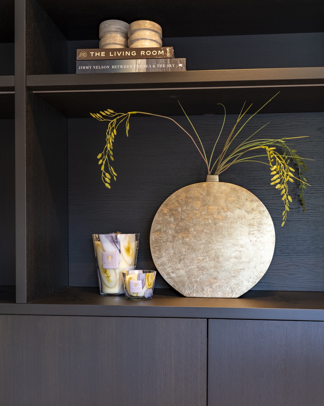 Luxe woonaccessoires en decoratieve vaas gestyled in een donkere maatwerkkast.