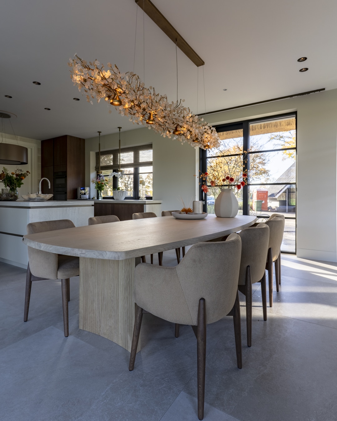 Ovale eettafel met zachte eetkamerstoelen in de woonkeuken van een nieuwbouwvilla.